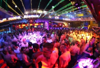Crowded Parrots Pub, a gay bar in Yumbo Centre, Maspalomas, Gran Canaria. Gay nightlife, travel destination. Men socializing, party atmosphere.