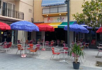 Parrots Pub terrace, a gay bar in Sitges. Outdoor seating with colorful umbrellas. A popular spot for gay men travel.