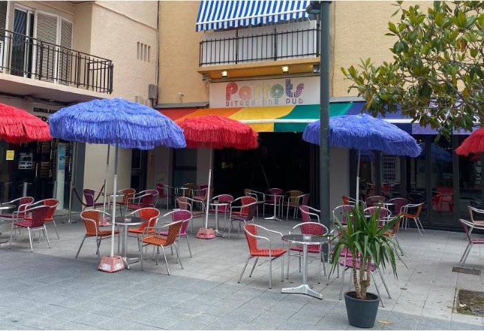 Parrots Pub terrace, a gay bar in Sitges. Outdoor seating with colorful umbrellas. A popular spot for gay men travel.
