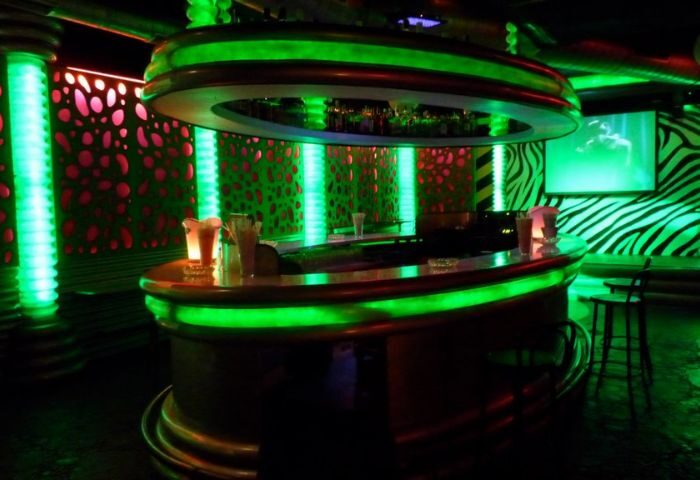 Interior of Parthenon Gay Cruise Club in Torremolinos. Bar area with green neon lights, zebra-striped wall, and modern design elements.