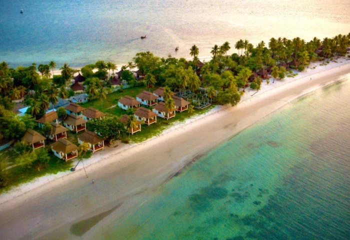 Pawapi Koh Mook Resort in Trang, Thailand. Aerial view of beach bungalows, palm trees, and turquoise water. Gay travel destination.