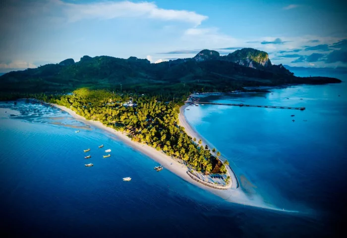 Aerial view of Pawapi Resort, Koh Mook, Trang. Tropical island with palm trees, sandy beaches, boats, and clear blue water. Gay travel destination.