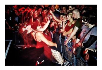 Peaches in Toronto performing for a crowd of fans. Gay men travel to Toronto to see live music. Red lighting, fishnets, and sunglasses.