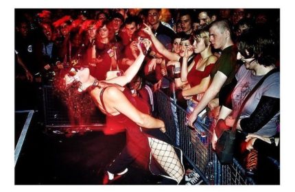 Peaches in Toronto performing for a crowd of fans. Gay men travel to Toronto to see live music. Red lighting, fishnets, and sunglasses.