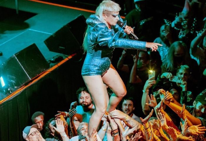 Peaches in Toronto: Singer crowd surfs at a concert. The queer artist is wearing a shiny blue outfit and singing into a microphone. Gay travel.