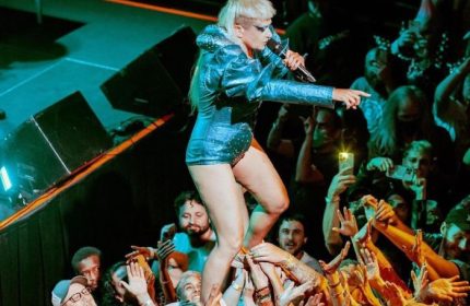 Peaches in Toronto: Singer crowd surfs at a concert. The queer artist is wearing a shiny blue outfit and singing into a microphone. Gay travel.