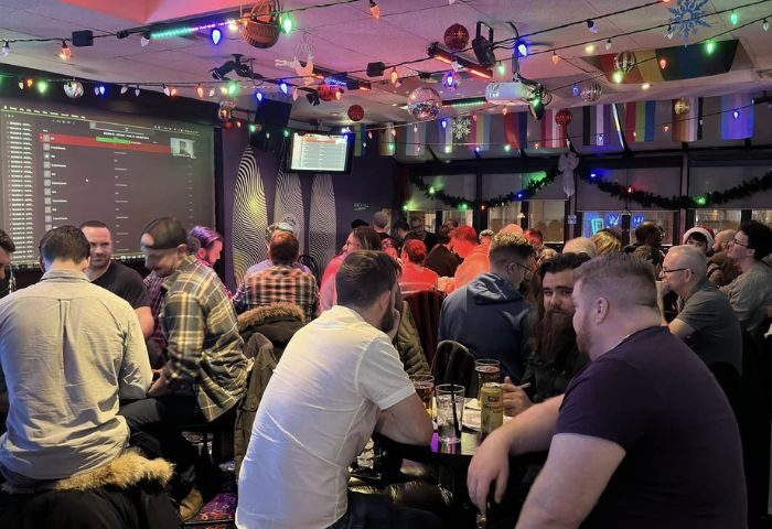 Interior shot of Pegasus on Church, a gay bar in Toronto, Canada. Men are seated at tables, with drinks. Festive lights decorate the ceiling.