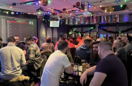 Interior shot of Pegasus on Church, a gay bar in Toronto, Canada. Men are seated at tables, with drinks. Festive lights decorate the ceiling.