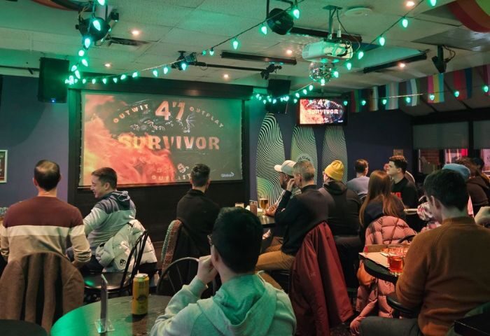 Pegasus On Church, a gay bar in Toronto. Patrons watch Survivor on a large screen. Green lights decorate the ceiling. A fun gay travel spot.