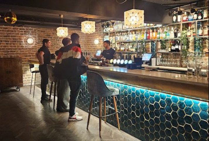 Interior shot of Penny Lane Gay Bar in Dublin. Bartender serving customers at a stylish bar with illuminated honeycomb pattern.