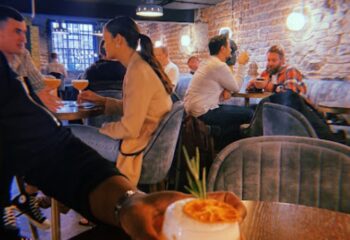 Patrons enjoy drinks at Penny Lane, a gay bar in Dublin. Brick walls, soft lighting, cocktails, and velvet seating create a cozy atmosphere.