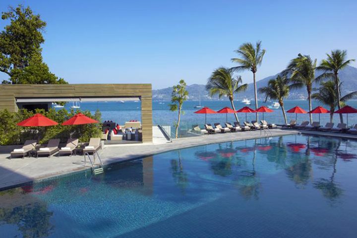 Amari Phuket beachfront gay hotel pool view. Thailand resort with palm trees, red umbrellas, and ocean view. Perfect for big group of friends.