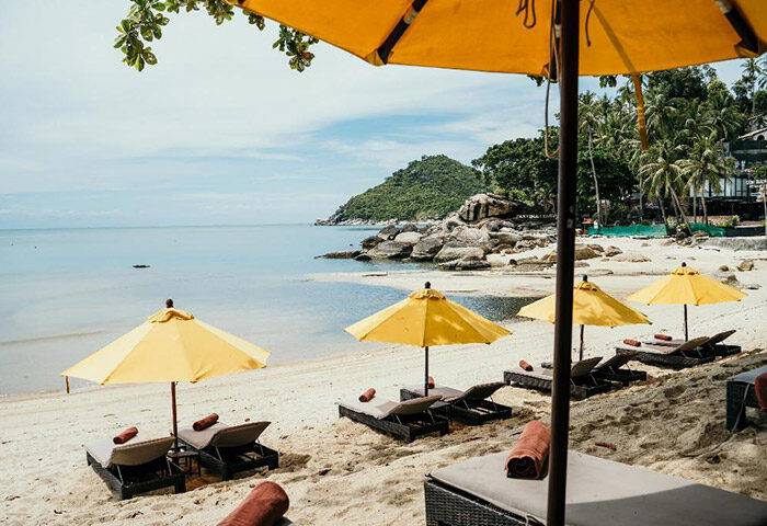Buri Rasa Koh Phangan beach view. Perfect gay honeymoon hotel. Yellow umbrellas and beach chairs on white sand. Tropical paradise.