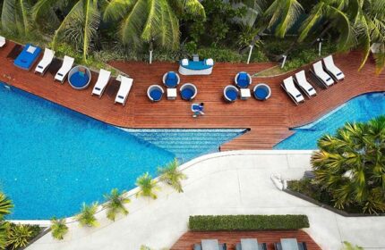 Baraquda Pattaya Mgallery hotel's pool area, perfect for a gay honeymoon. Aerial view of the pool, deck chairs, and lounge seating.