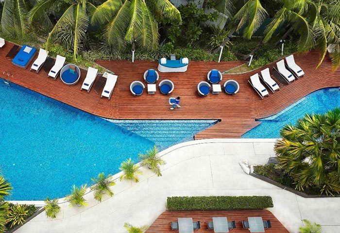 Baraquda Pattaya Mgallery hotel's pool area, perfect for a gay honeymoon. Aerial view of the pool, deck chairs, and lounge seating.