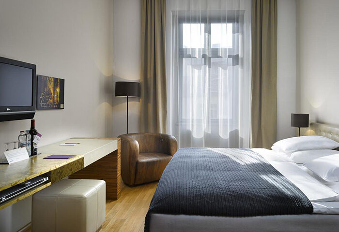 The Icon Hotel and Lounge room in Prague Old Town. Gay honeymoon hotel with bed, chair, desk, TV, wine, and window.