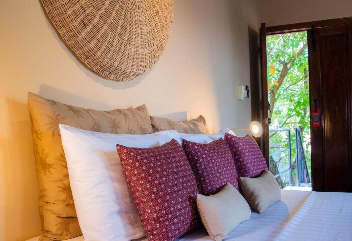 Rambutan Resort Siem Reap bedroom. Gay honeymoon hotels near gay bars in Siem Reap. Cozy bed with decorative pillows and open door to nature.