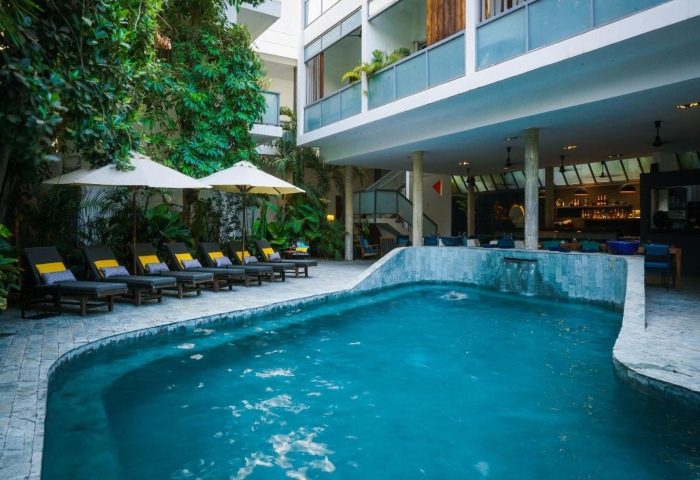 Rambutan Resort Phnom Penh pool view. Perfect gay honeymoon hotels in Phnom Penh. Loungers, umbrellas, and lush greenery surround the pool.