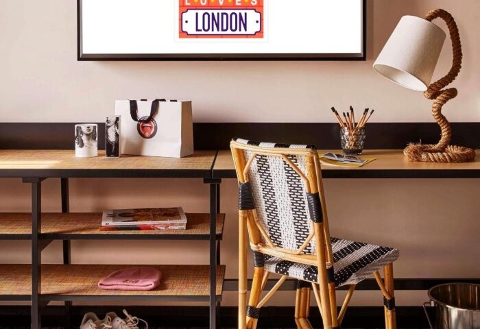 Mama Shelter London Shoreditch hotel room for solo gay travelers. Desk with chair, lamp, and TV displaying London Loves sign. Stylish decor.