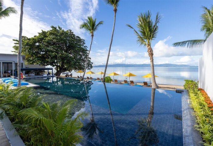 Koh Phangan's beachfront adults-only resort pool. Gay travel goals: palm trees, yellow umbrellas, and ocean views at Explorar Resort.