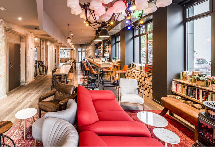 Les Piaules hostel in Paris' gayborhood: Stylish lounge area with red sofa, armchairs, bar, and communal tables. Perfect for solo gay travelers.