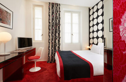 Hotel du Petit Moulin, a perfect Instagram hotel for gay travelers in Marais, Paris. Stylish room with red carpet, bed, desk, and patterned decor.