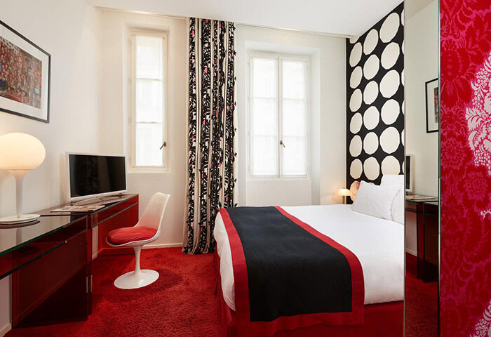 Hotel du Petit Moulin, a perfect Instagram hotel for gay travelers in Marais, Paris. Stylish room with red carpet, bed, desk, and patterned decor.