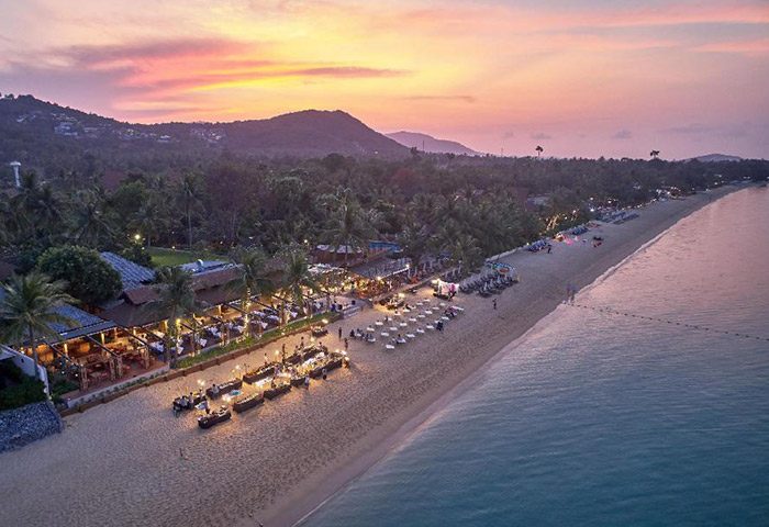 Bandara Resort & Spa, Koh Samui. Beachfront view of the gay-friendly hotel at sunset. Perfect private beach with dining and lounge areas.