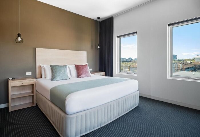 Saint Kilda Beach Hotel room, perfect for a gay honeymoon in Melbourne. Queen bed, bedside tables, and windows with city views. Modern, comfortable.