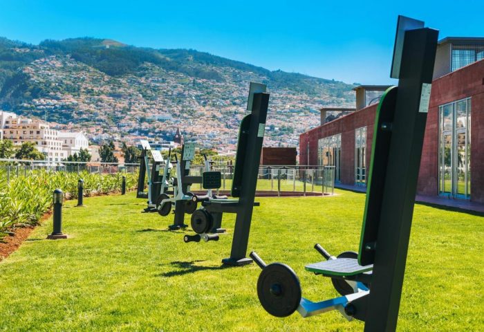 Outdoor gym at Pestana CR7 Hotel, Madeira. Fitness equipment on green lawn with mountain view. Gay travel, active vacation.
