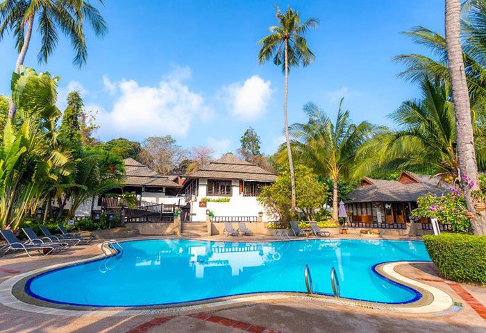 Phi Phi Holiday Resort pool view. Beachfront gay hotel with pool, cheap price. Tropical trees, blue sky, and inviting water.