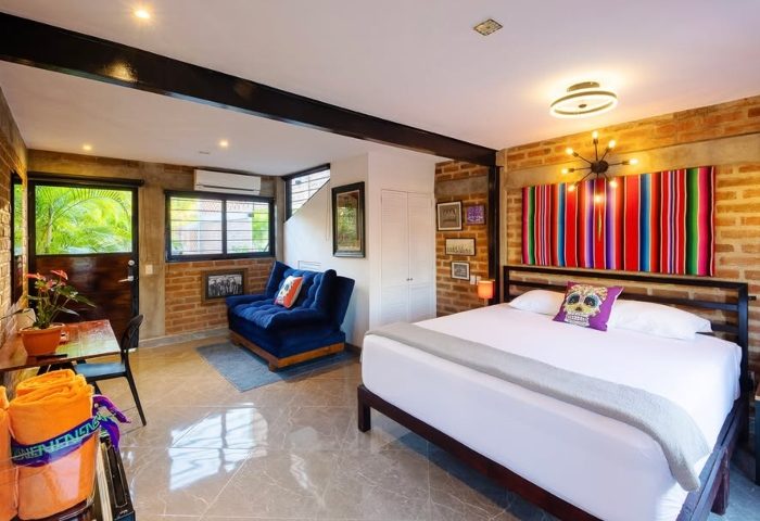 Piñata PV Gay Hotel room. Modern design with brick walls, colorful blanket, skull pillow, and blue sofa. Gay travel in Puerto Vallarta.