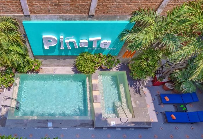 Aerial view of Piñata PV Gay Hotel pool and lounge area in Puerto Vallarta. Tropical plants and blue lounge chairs.