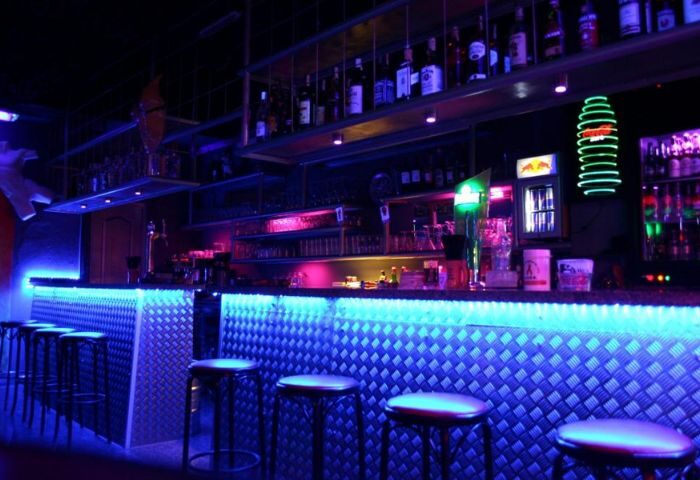 Pirates Bar, a gay bar in Gran Canaria, features a bar with blue LED lighting and stools. Shelves of liquor bottles are visible.