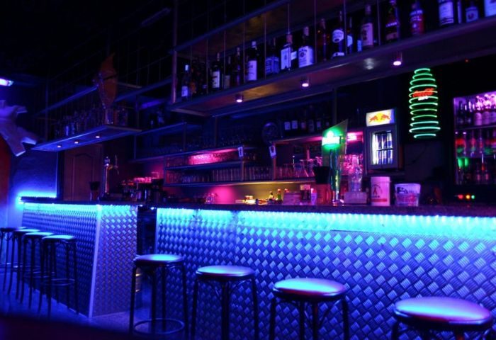 Pirates Bar, a gay bar in Gran Canaria, features a bar with blue LED lighting and stools. Shelves of liquor bottles are visible.