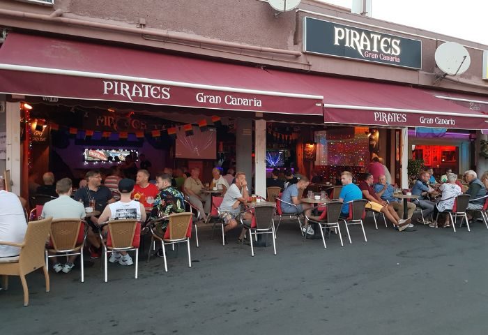 Pirates Bar Gran Canaria, a popular gay bar in Gran Canaria, Spain. Men sit at tables outside under a red awning, enjoying drinks.