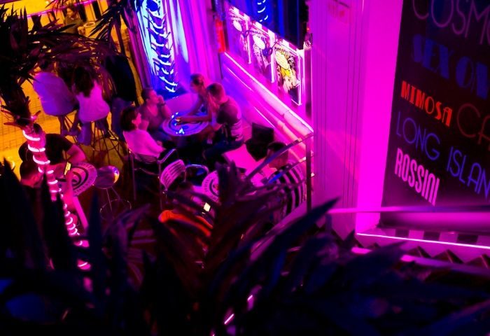 Plata Cocktail Bar, a gay bar in Barcelona. People at tables, neon lights, and cocktail menu. A vibrant nightlife scene.