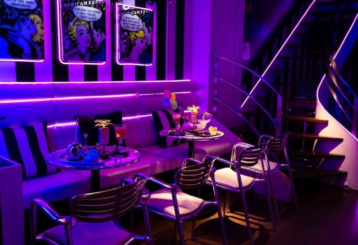 Interior of Plata Cocktail Bar, a gay bar in Barcelona, featuring purple neon lighting, cocktail tables, and stylish seating for gay travelers.