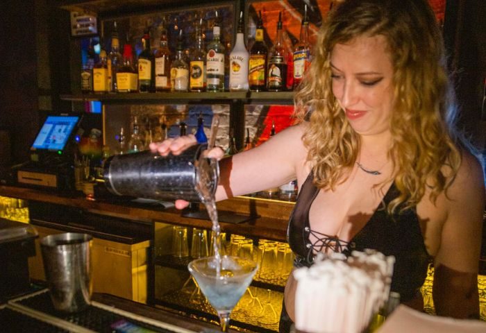 Bartender pouring cocktail at Playhouse Gay Bar in New York. Woman with curly hair making a drink. Gay nightlife travel.