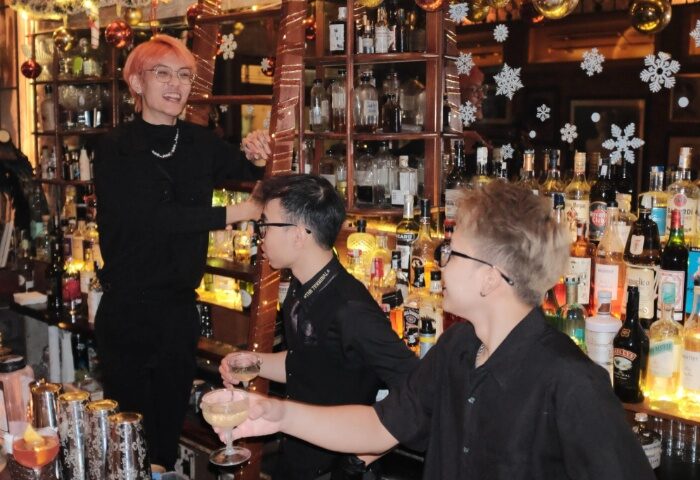 Polite & Co, Hanoi. Gay bar scene with bartenders in black shirts, drinks, and shelves of liquor. Gay travel advice in Vietnam.