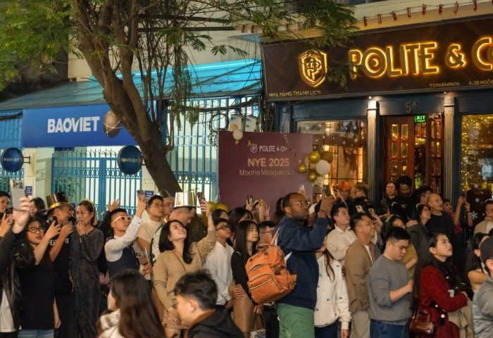 Polite & Co. Hanoi crowd celebrates NYE 2025. Gay travel advice: a diverse group of people, some with party hats, capture the moment with phones.
