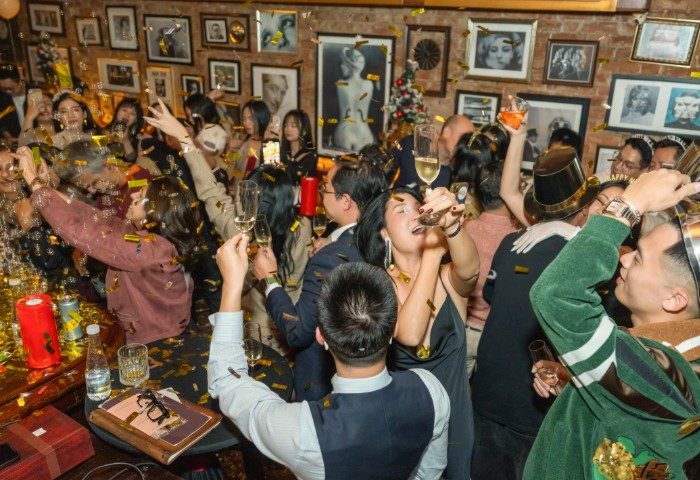 Polite & Co Hanoi: Gay men celebrate with champagne and confetti in a bar with framed photos. Gay travel advice for Hanoi nightlife.