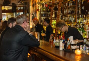 Polite & Co Hanoi bar scene. Bartenders serve drinks to patrons at the bar. Gay travel advice. Nightlife in Vietnam.