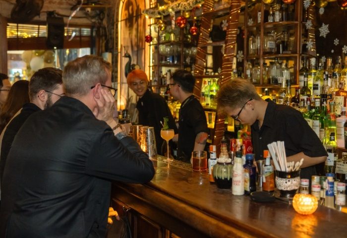 Polite & Co Hanoi bar scene. Bartenders serve drinks to patrons at the bar. Gay travel advice. Nightlife in Vietnam.
