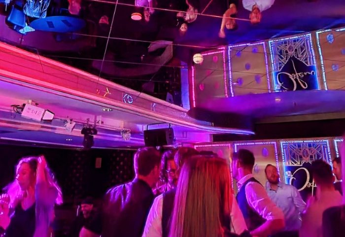 Inside Polygon Club Budapest: Gay men enjoy the vibrant nightlife. Pink and blue lights illuminate the dance floor. A mirrored ceiling reflects the party.