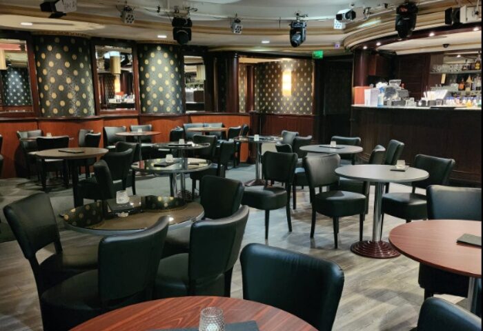 Interior of Polygon Club Budapest, a gay bar. Tables and chairs fill the space, with a bar in the background, ready for a night out.