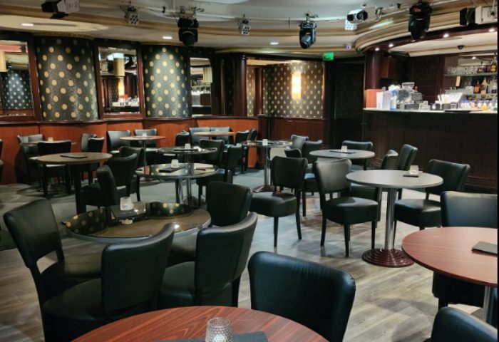 Interior of Polygon Club Budapest, a gay bar. Tables and chairs fill the space, with a bar in the background, ready for a night out.