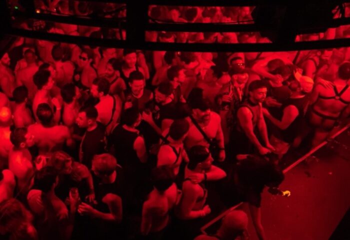 Red-lit crowd at Poof Doof, a gay dance party in Melbourne, Australia. Men in harnesses dance. Gay travel advice.