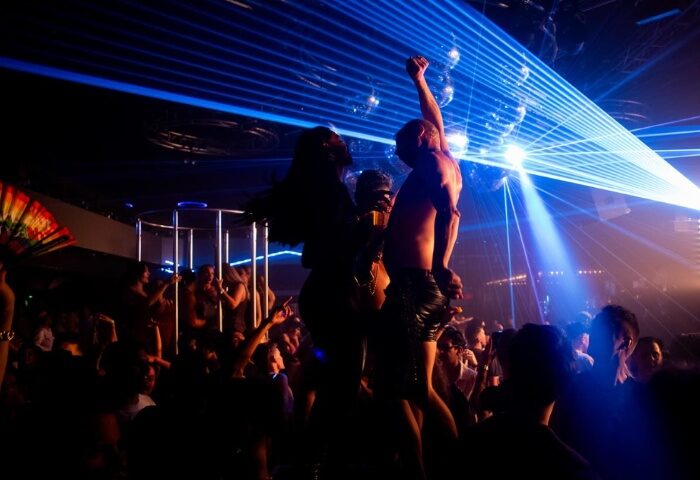 Poof Doof Melbourne: Gay men dancing in a nightclub with laser lights and disco balls. Partygoers enjoying the vibrant atmosphere.