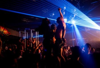 Poof Doof Melbourne: Gay men dancing in a nightclub with laser lights and disco balls. Partygoers enjoying the vibrant atmosphere.